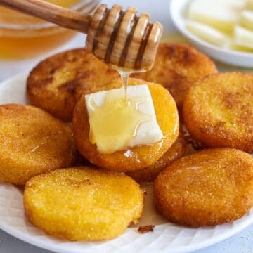  Südliches Heißwassermaisbrot auf einem Teller mit Butter und Honig, die darauf geträufelt werden, und mehr Honig und Butter im Hintergrund.