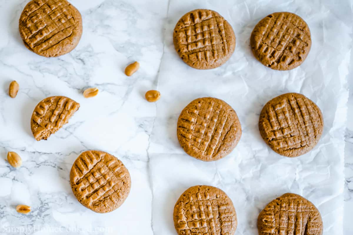 Easy Keto Peanut Butter Cookies on a white background, one broken with some peanuts nearby.