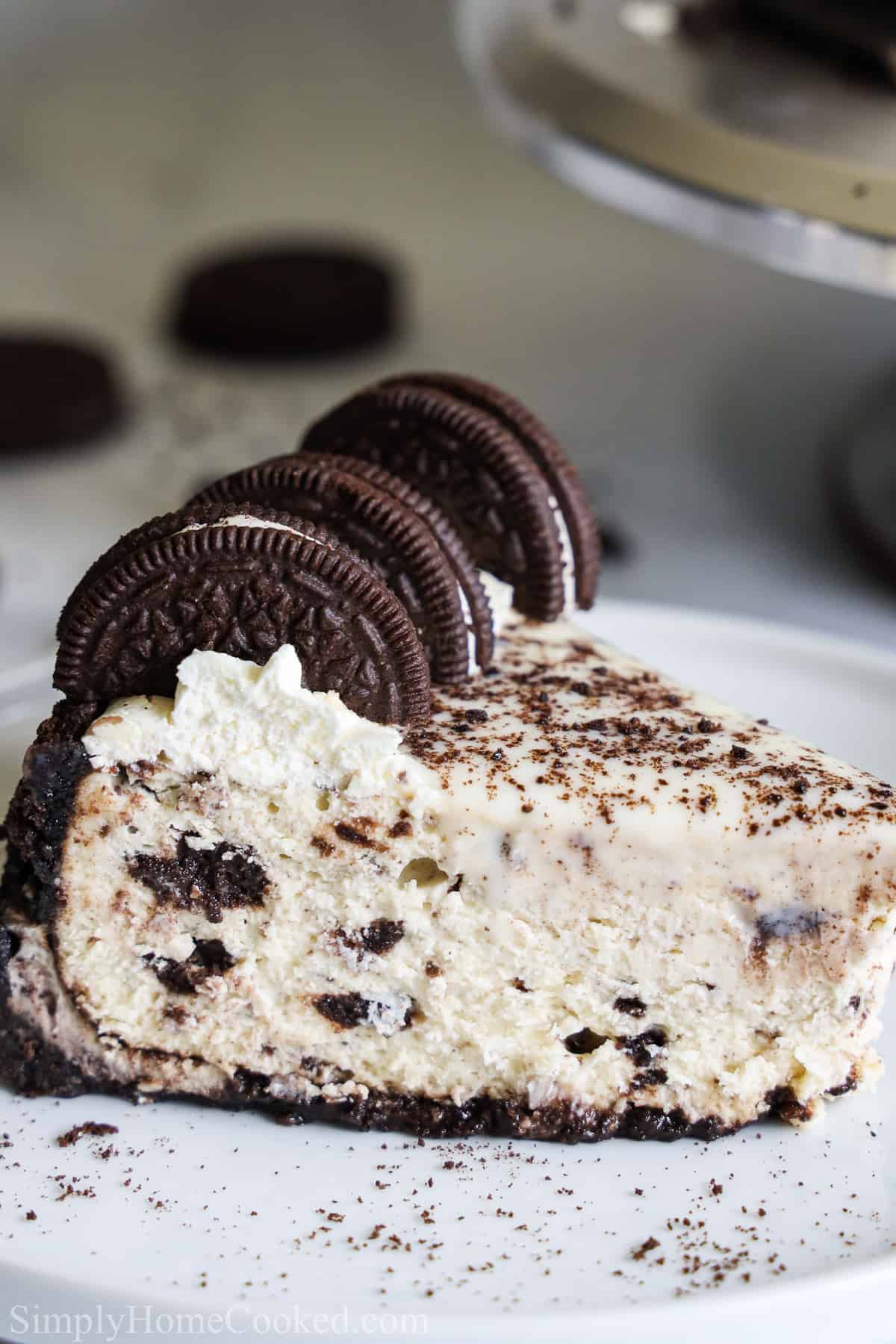 Close up side view of a slice of Easy Oreo Cheesecake with Oreos on top, on a white plate.