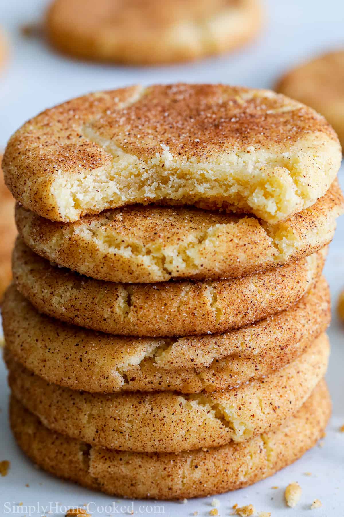 Close up of a stack of Soft Snickerdoodle Cookies with a bite taken out of the top one, more cookies in the background.