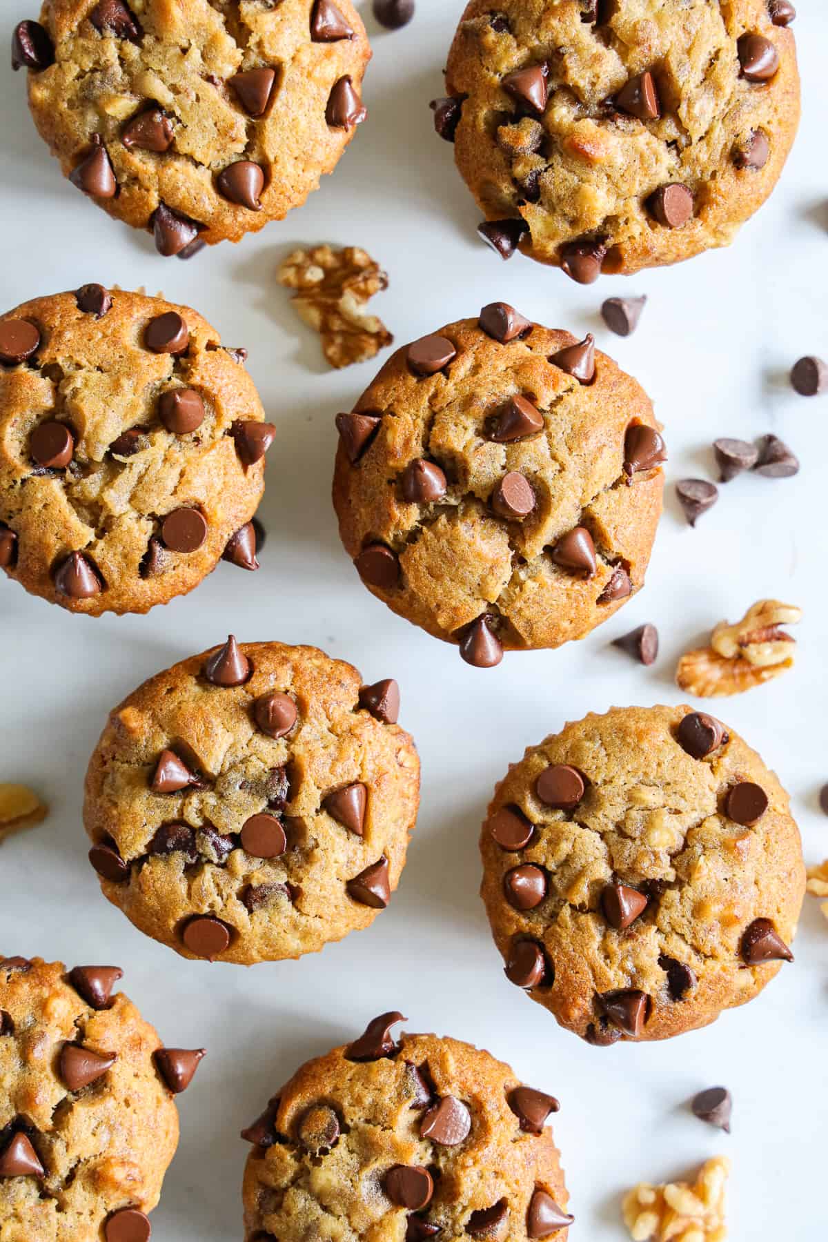 Overhead view of Banana Chocolate Chip Muffins with chocolate chips and walnuts scattered around them.