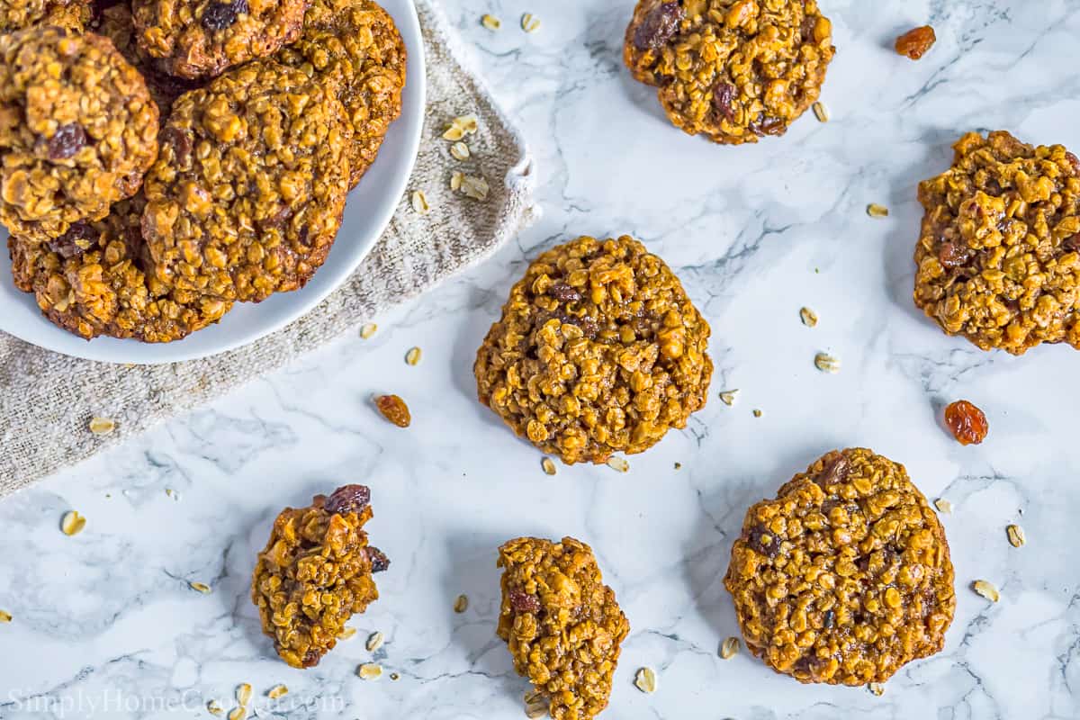 Chewy Oatmeal Raisin Cookies on a white plate with a few more cookies scattered nearby and some broken cookies and crumbs.