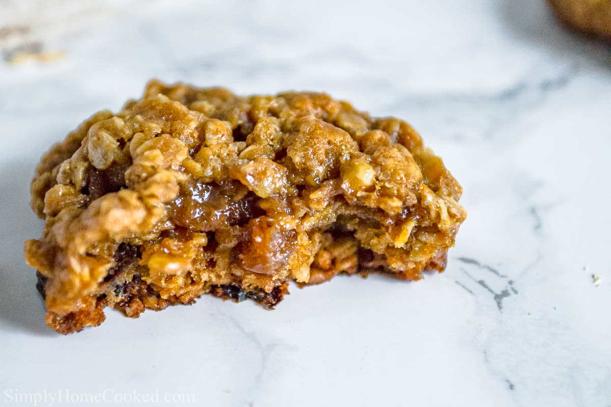 A Chewy Oatmeal Raisin Cookie missing a few bites on a white background.