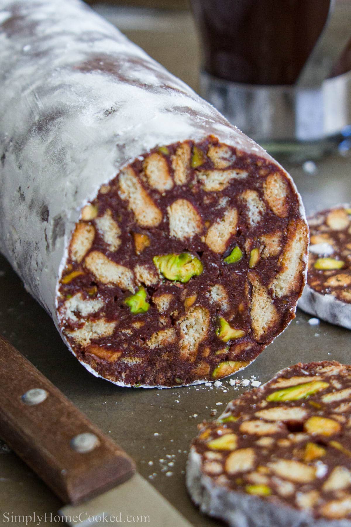 A stick of chocolate salami with a slice of it sliced of and a knife beside it.