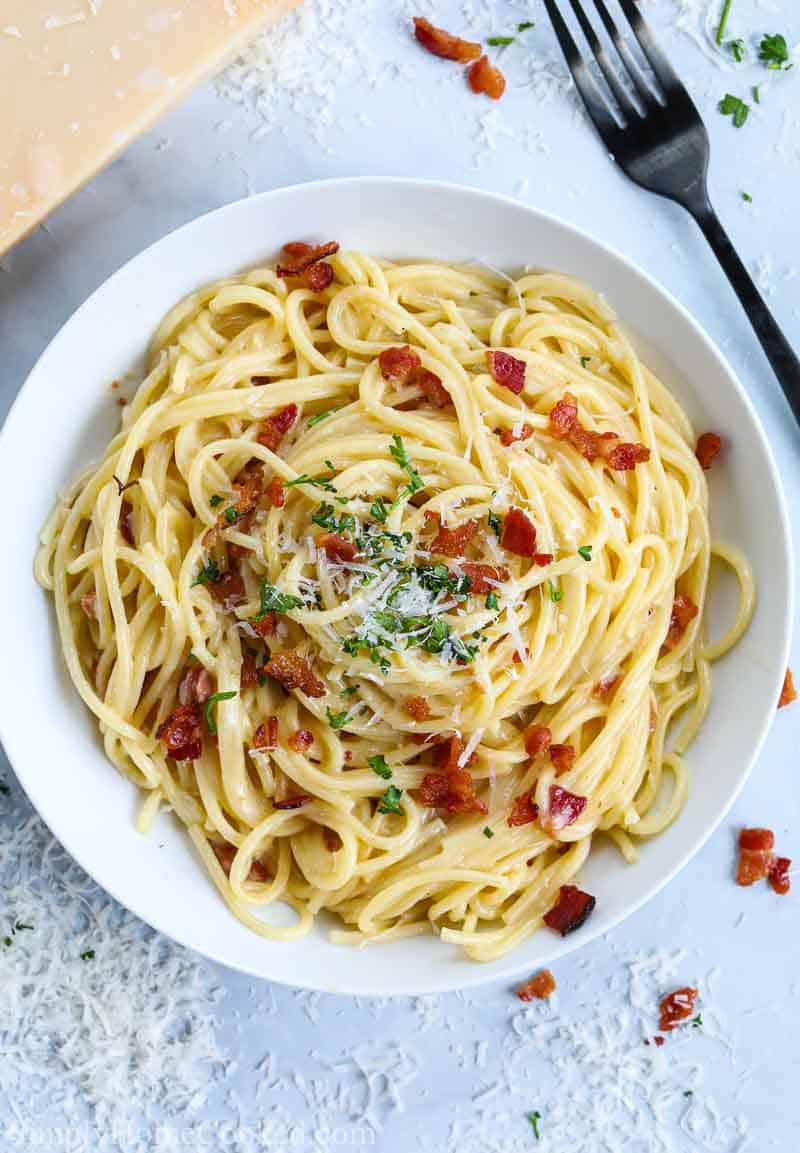 close up image of spaghetti carbonara in a white dish with grated parmesan, bacon, and parsley on top