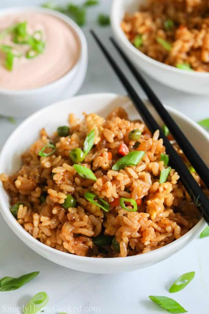 Bowl of Hibachi Fried Rice with chopsticks on the side and another bowl in the background with some yum yum sauce.