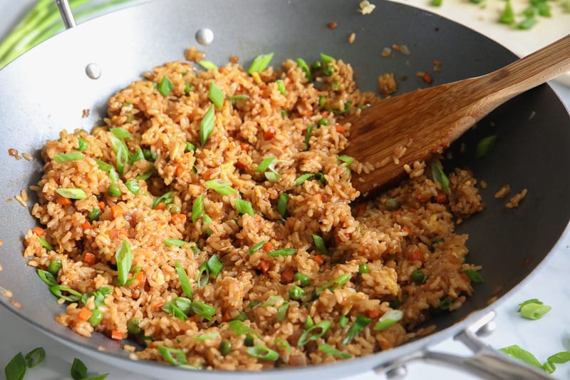 Hibachi Fried Rice in a wok with green onion and a wooden spoon.