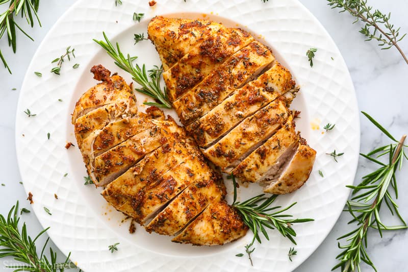 Juicy Air Fryer Chicken Breast on a white plate with rosemary garnish.