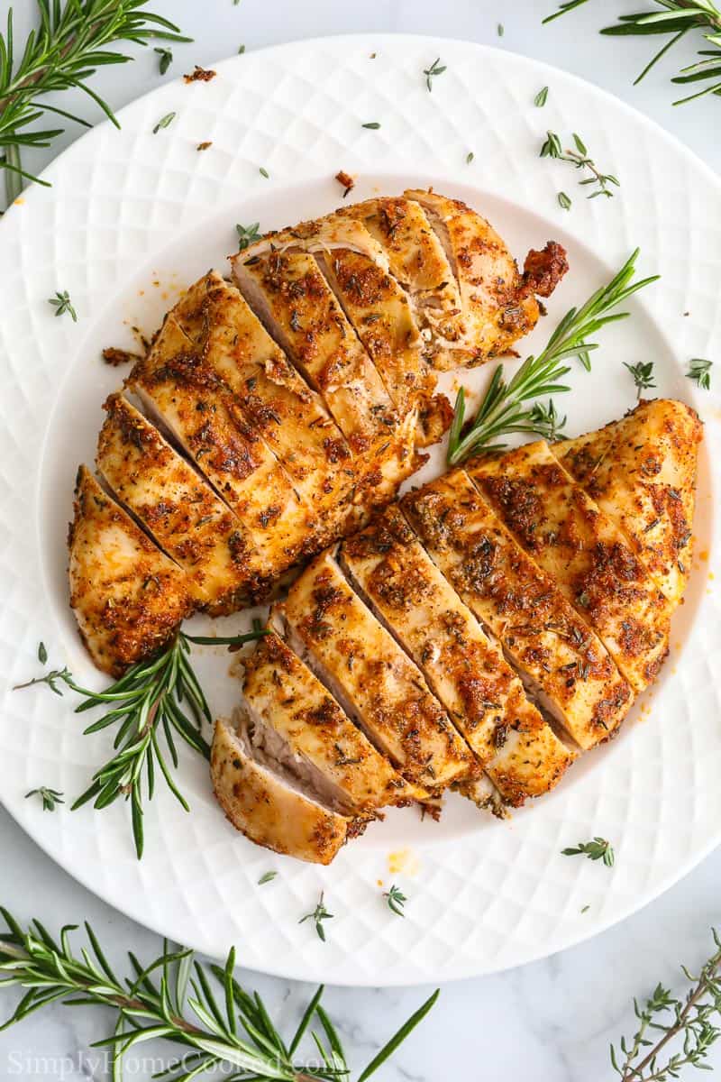 Close up of Juicy Air Fryer Chicken Breast on a white plate with rosemary garnish.