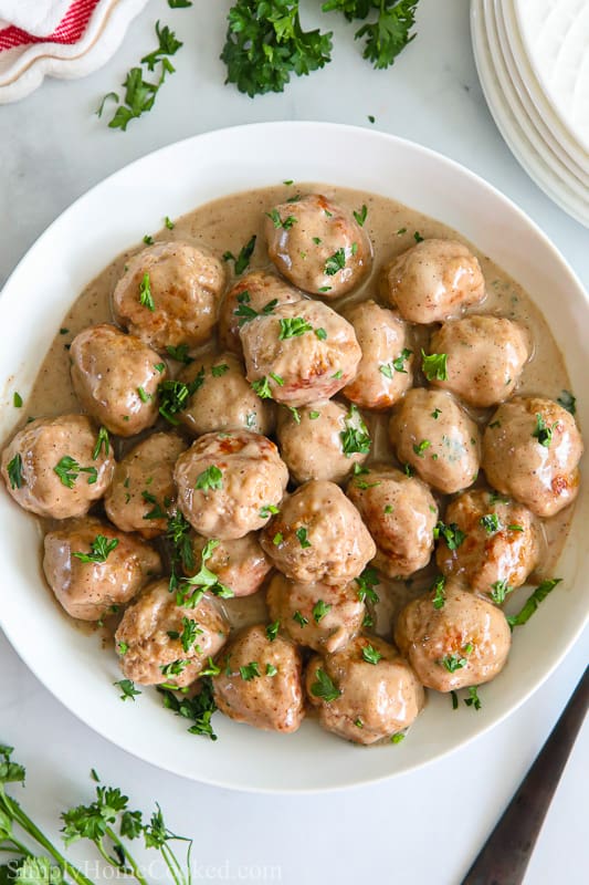 Overview of a white bowl filled with Perfect Swedish Meatballs sprinkled with parsley.