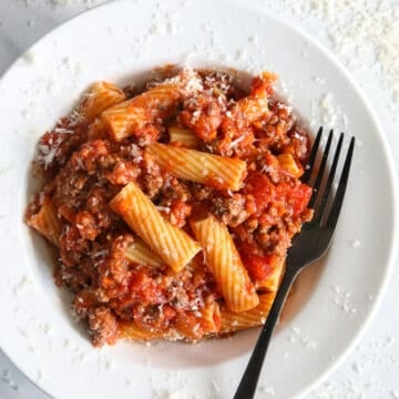 Plate of Rigatoni Bolognese with a fork and grated Parmesan cheese.