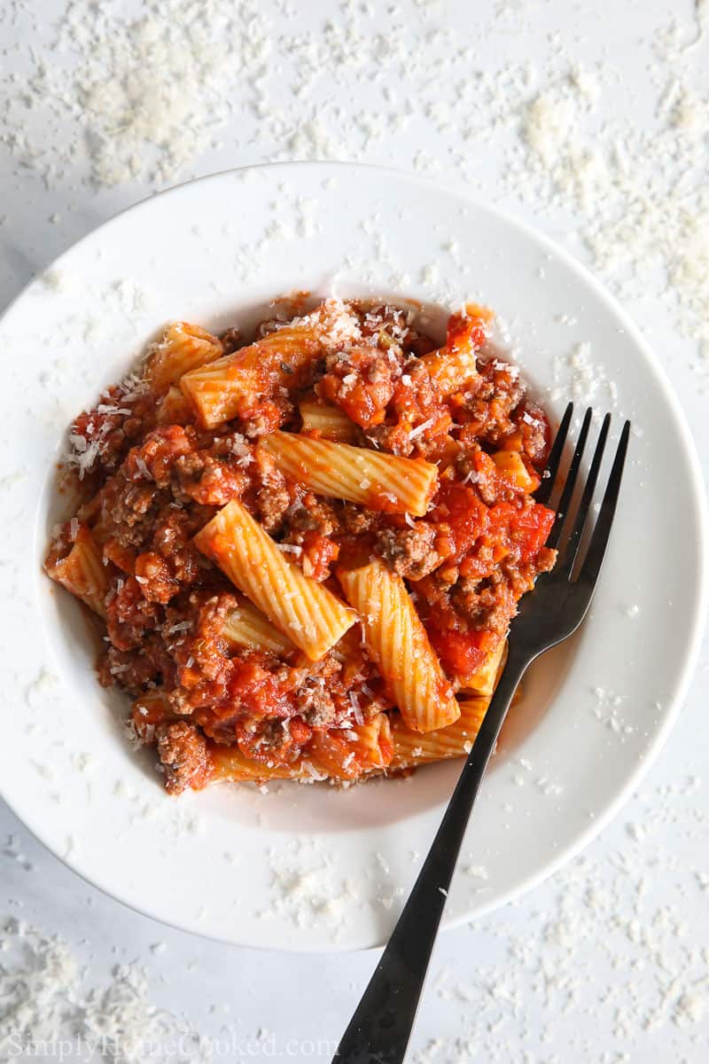 Plate of Rigatoni Bolognese with a fork and grated Parmesan cheese.
