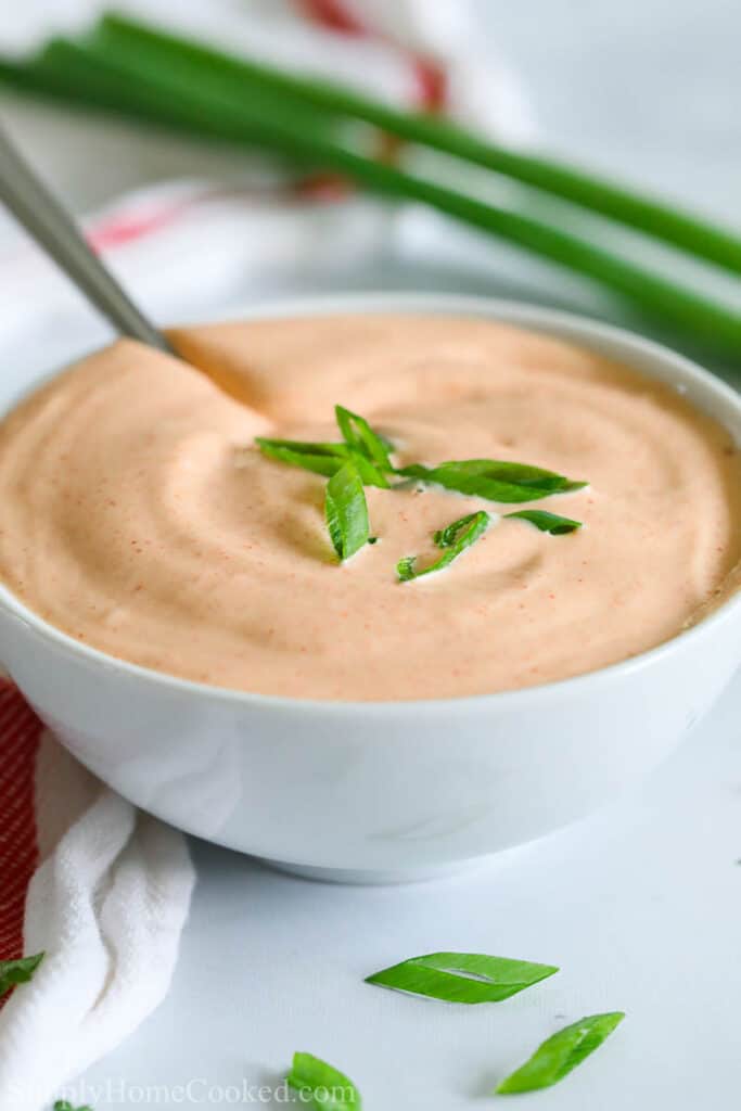 close up image of homemade yum yum sauce in a white bowl with chopped green onion on top