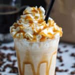 Caramel frappuccino with whipped cream, caramel sauce, and a straw, with coffee beans in the background.