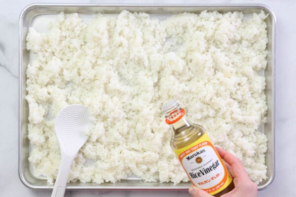 Steps to make California Roll Sushi Bowls: cook the rice and then use a rice paddle to mix it with rice vinegar.