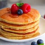 close up image of a stack of almond flour pancakes on a white plate with berries and syrup on top