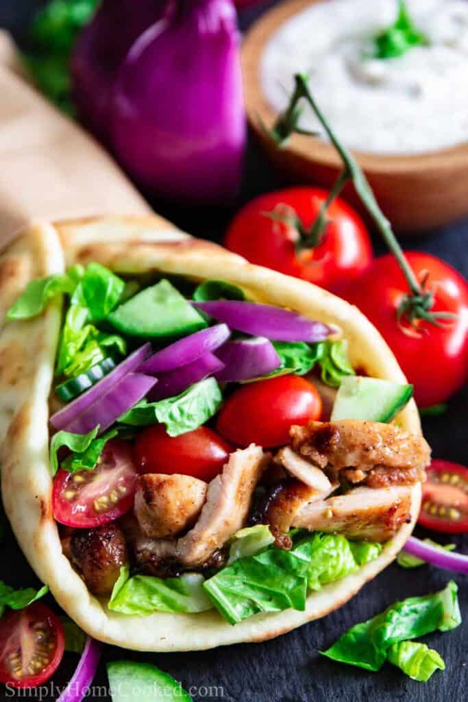 Chicken Shawarma in a pita with vegetables and yogurt sauce nearby
