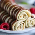 Close up of rolled crepes stacked and drizzled with chocolate sauce
