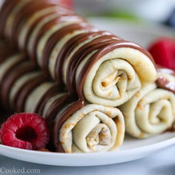A close-up of rolled crepes stacked and dipped in chocolate sauce