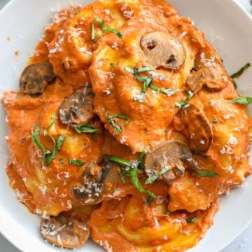 overhead image of sausage ravioli in a white plate with mushrooms and basil beside it