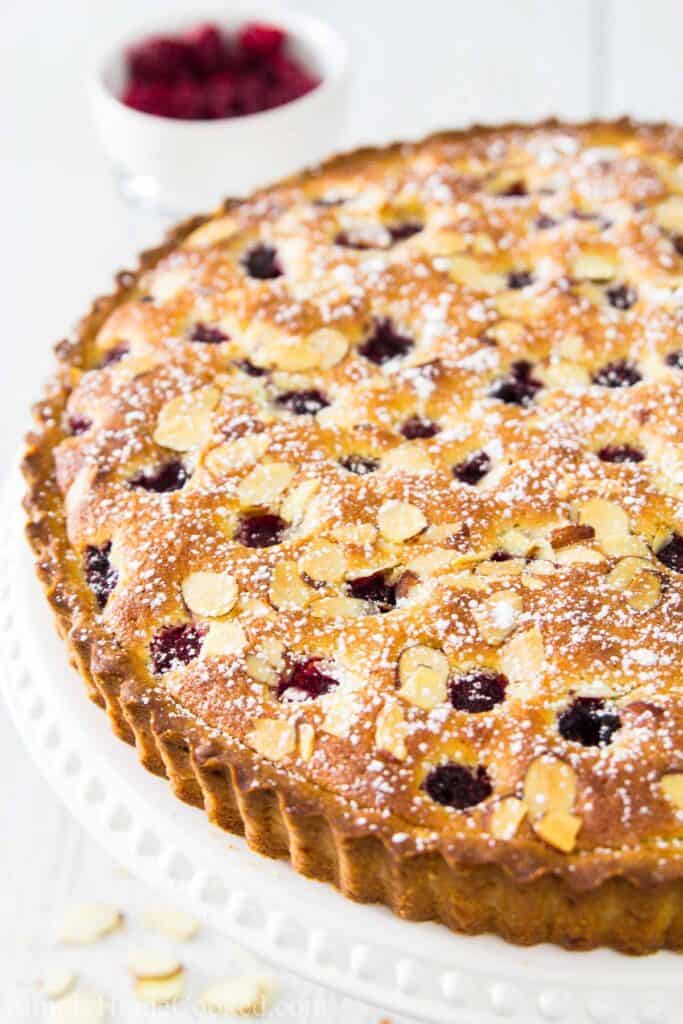 Bakewell Tart dusted with powdered sugar and raspberries in the background