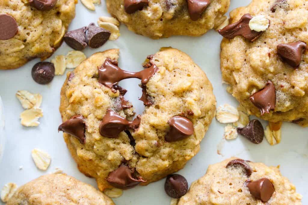 These Chewy Banana Oatmeal Cookies are the perfect sweet treat. Bananas, brown sugar, and oats - you're going to love this soft, yummy dessert. #bestoatmealcookies #bestchewyoatmealcookies #chewybananaoatmealcookierecipe #chewyoatmealcookierecipe close up overhead image of a banana oatmeal cookie being pulled apart with melted chocolate chips oozing out