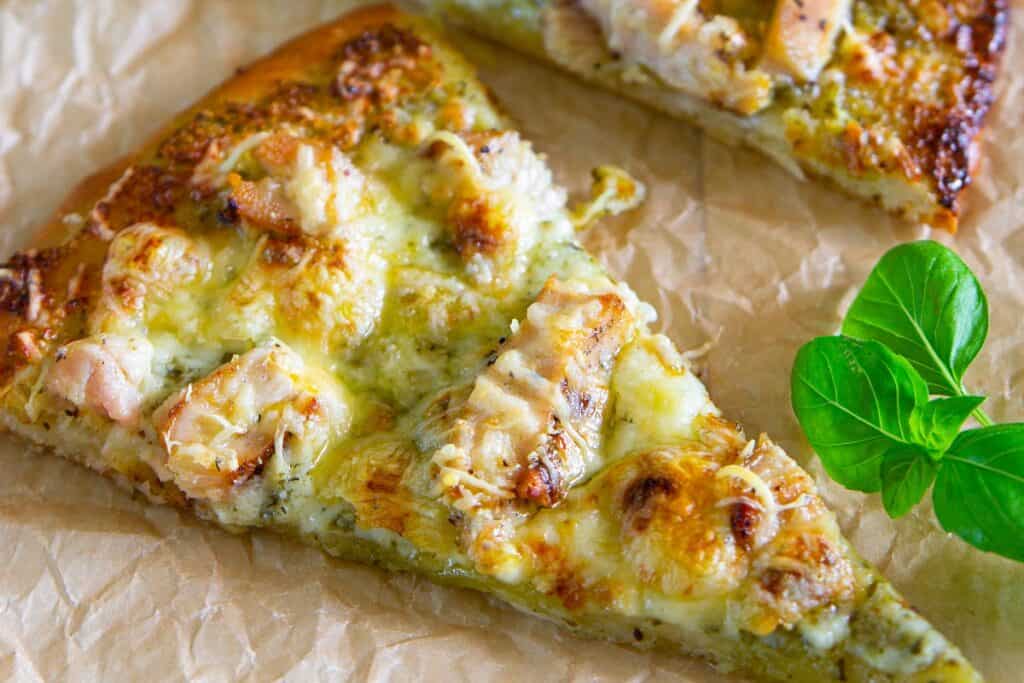 Slices of Chicken Pesto Pizza with basil nearby
