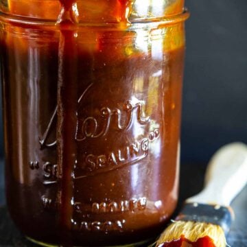 Vertical image of Homemade Barbecue Sauce in a mason jar with a brush nearby