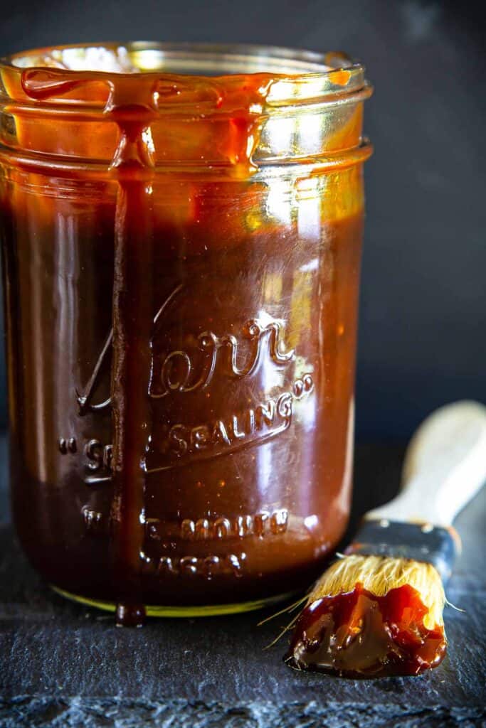 Vertical image of Homemade Barbecue Sauce in a mason jar with a brush nearby