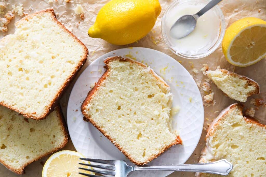 overhead image of a slice of lemon pound cake on a white plate with lemon and crumbs around it