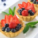 Mini Fruit Tarts lined up on a plate with blueberries in the background.