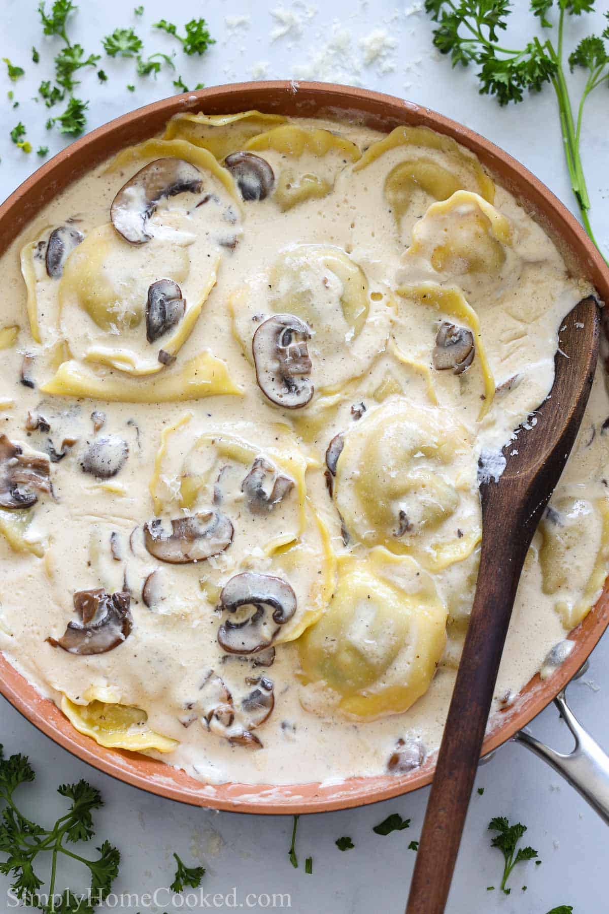 Vertical image of a pan of Mushroom Ravioli with a wooden spoon