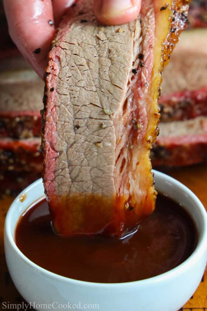 Vertical image of a slice of Smoked Beef Brisket being dipping into barbecue sauce.