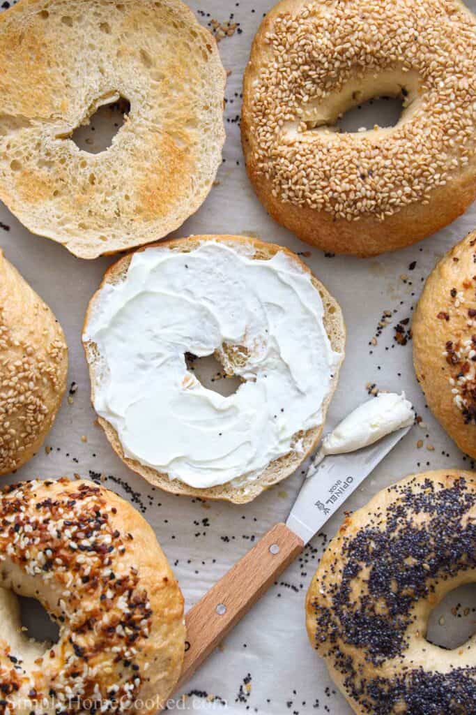 Sourdough bagels with different toppings, one spread with cream cheese, and a knife.