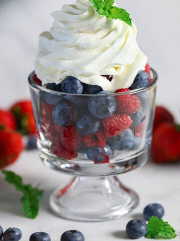 Vertical image of cup of fresh berries with Chantilly Cream on top
