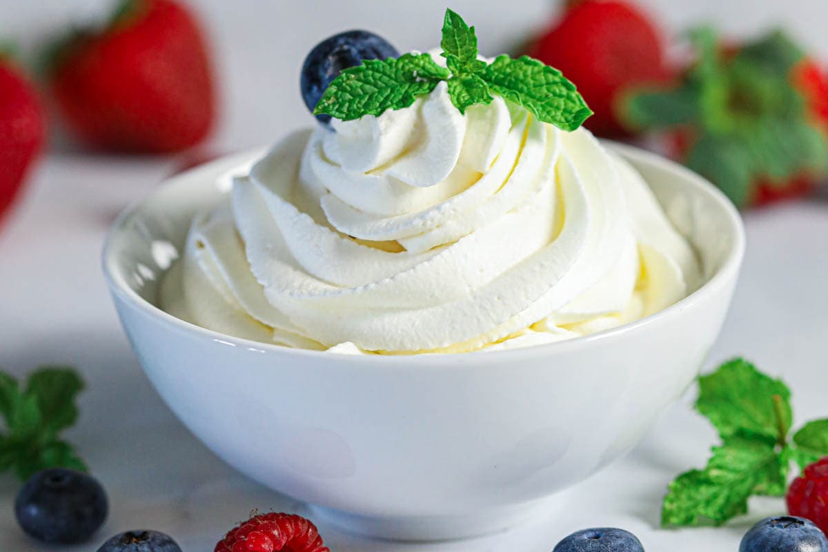 Bowl of Chantilly Cream with mint leaf garnish and berries in the background