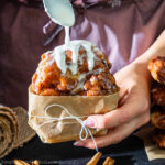 close up image of an apple fritter getting glazed with a spoonful of icing