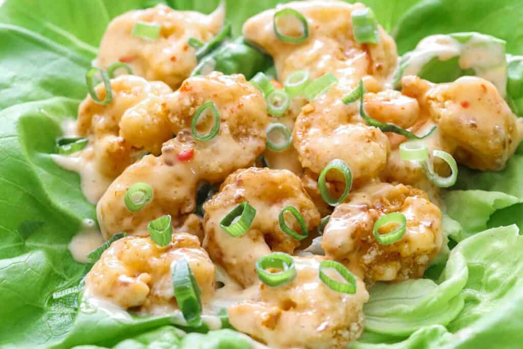 Horizontal image of Bang Bang Shrimp on a bed of butter lettuce with green onion garnishing the top