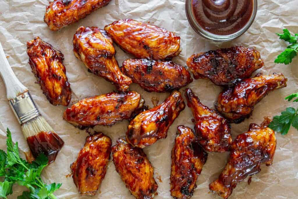 Horizontal image of Easy BBQ Wings scattered on parchment paper with barbecue sauce.