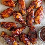 square image of BBQ Wings scattered on parchment paper with barbecue sauce.