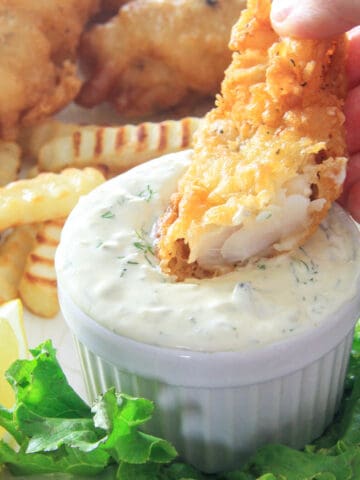 Beer Battered Cod being dipped in tartar sauce with fries in the background.