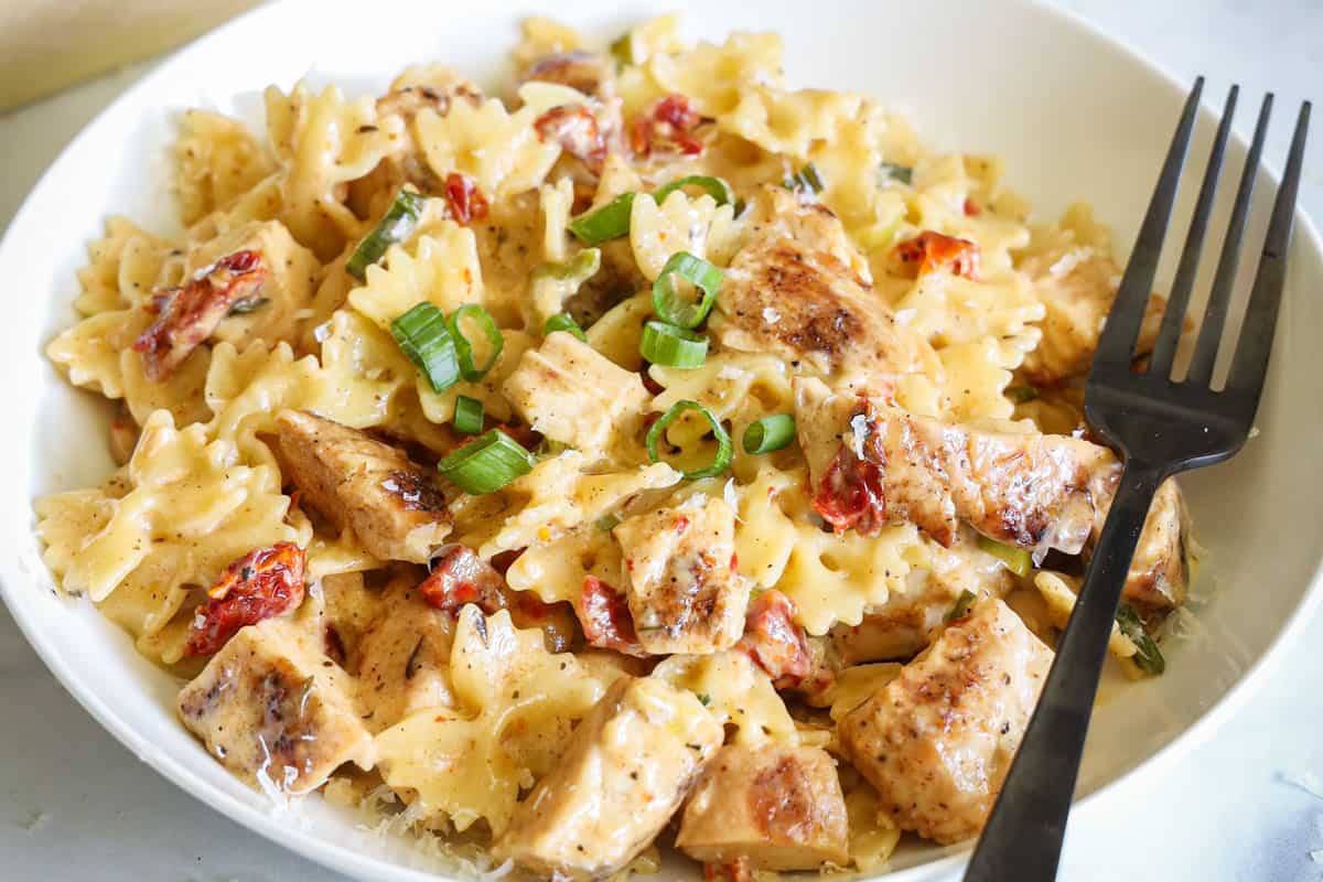 Horizontal image of plate of Blackened Chicken Alfredo garnished with green onion and a fork on the side