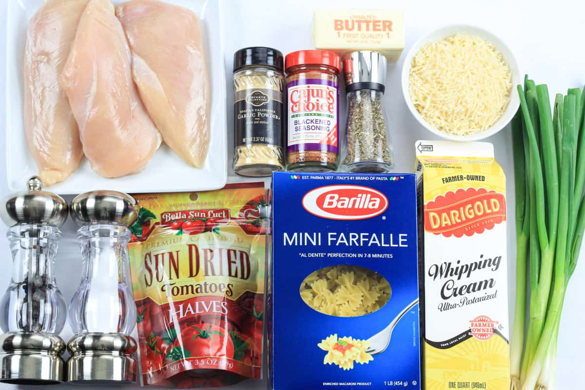 Ingredients for Blackened Chicken Alfredo, including pasta, whipping cream, chicken, sun-dried tomatoes, butter, green onion, Parmesan cheese, and seasonings.