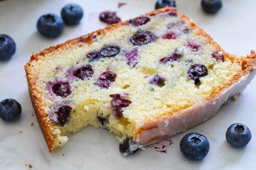 horizontal image of a slice of blueberry bread with fresh blueberries around it