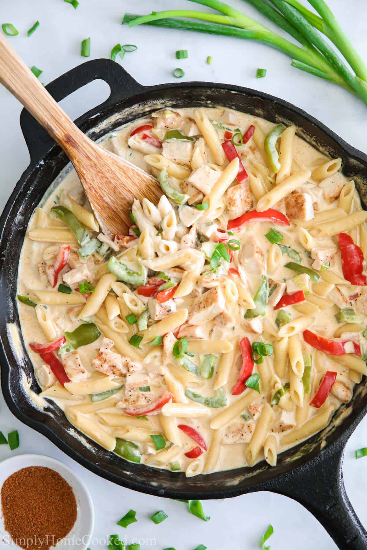 Vertical image of Cajun Chicken Alfredo in a skillet with a wooden spoon