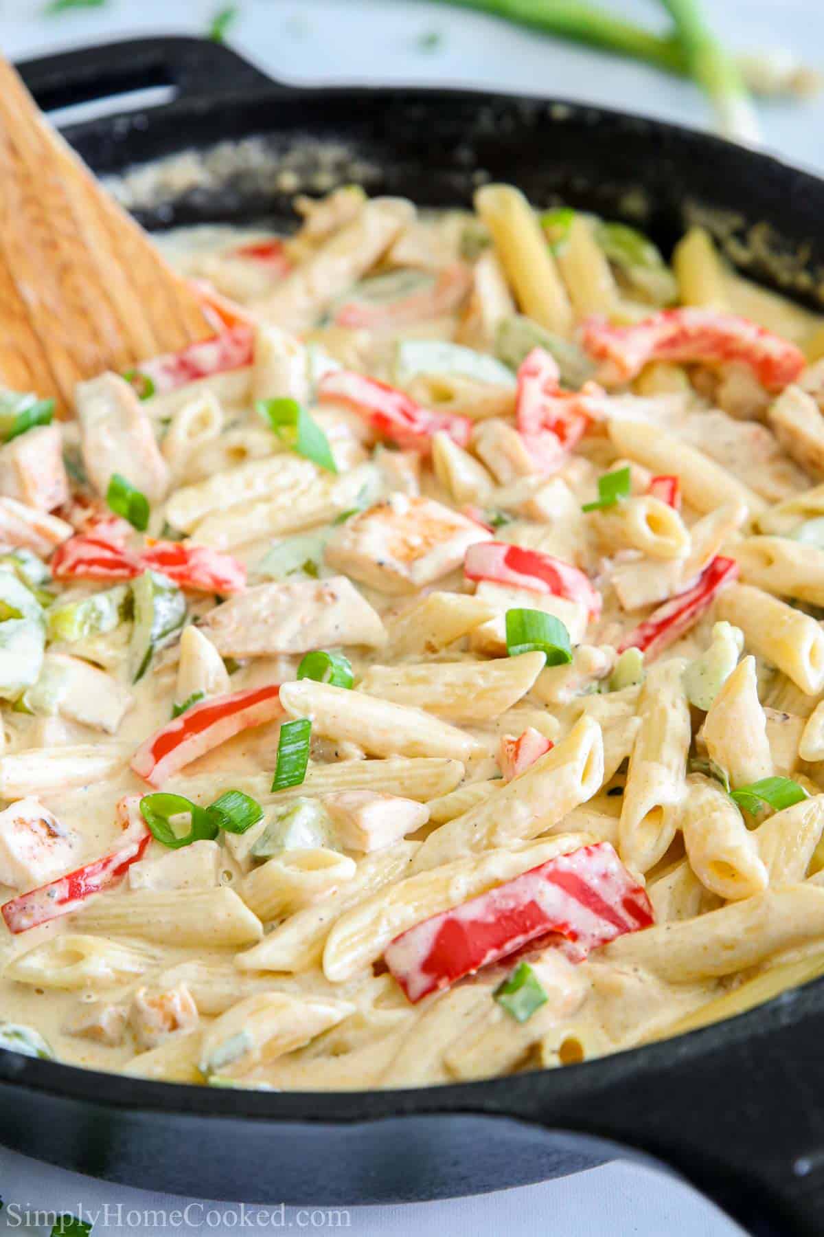 Close up of Cajun Chicken Pasta in a skillet with a wooden spoon stirring it.