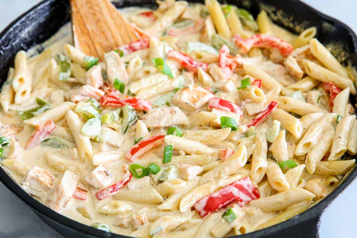 Horizontal image of Cajun Chicken Alfredo in a skillet with a wooden spoon stirring.