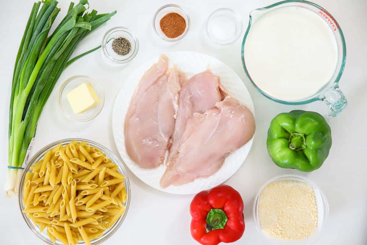 Ingredients for Cajun Chicken Pasta, including chicken breasts, green onions, green and red peppers, penne, heavy cream, Parmesan cheese, butter, salt, pepper, and Cajun seasoning.