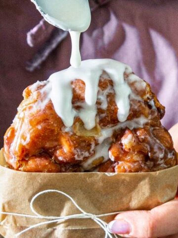 close up image of an apple fritter getting glazed with a spoonful of icing