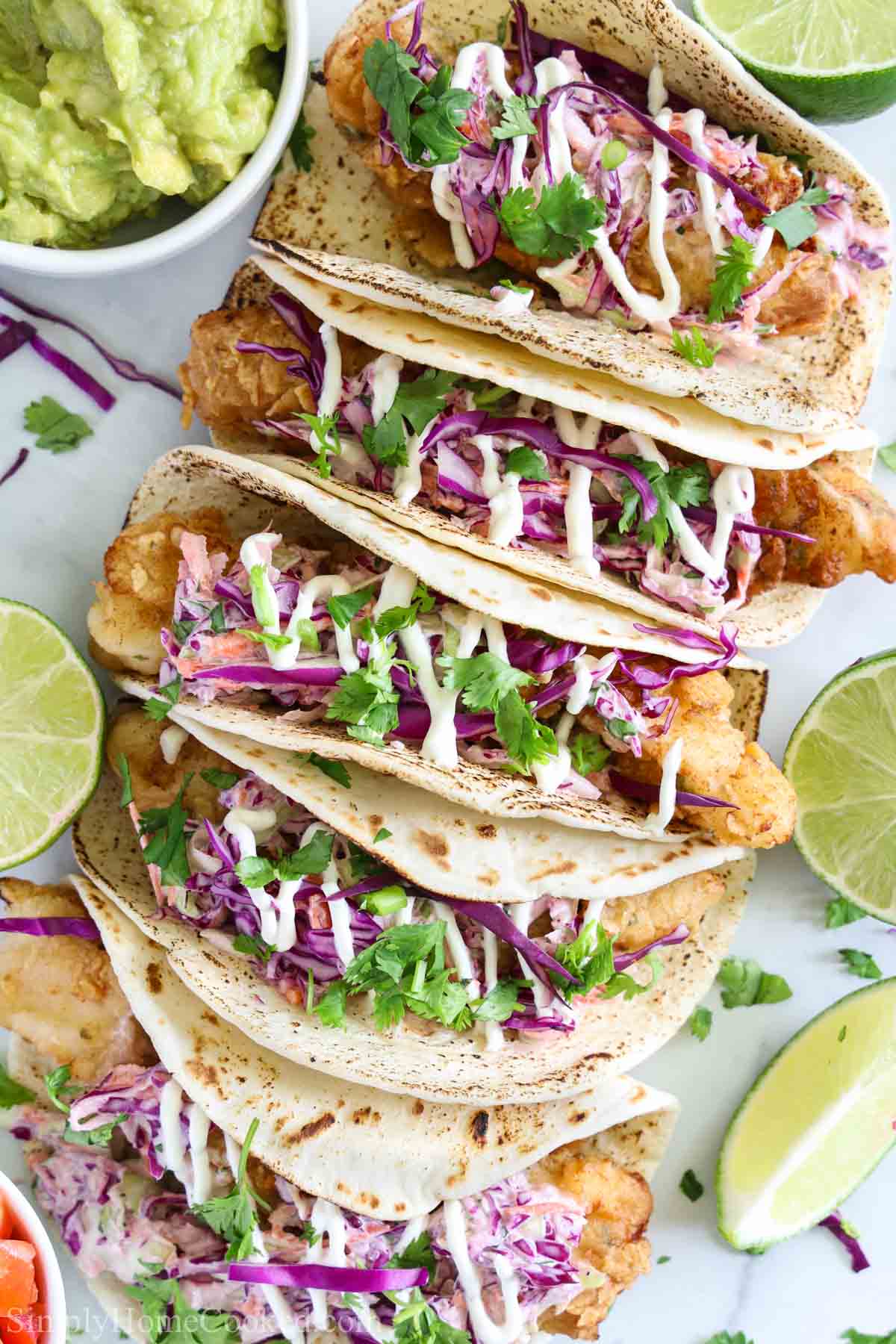Row of Fish Tacos with limes and guacamole on the side